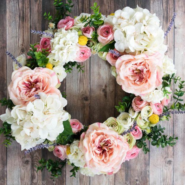 Round faux flower wreath of blush roses, white hydrangeas, ranunculus, yellow billy buttons and lavender on grey wood