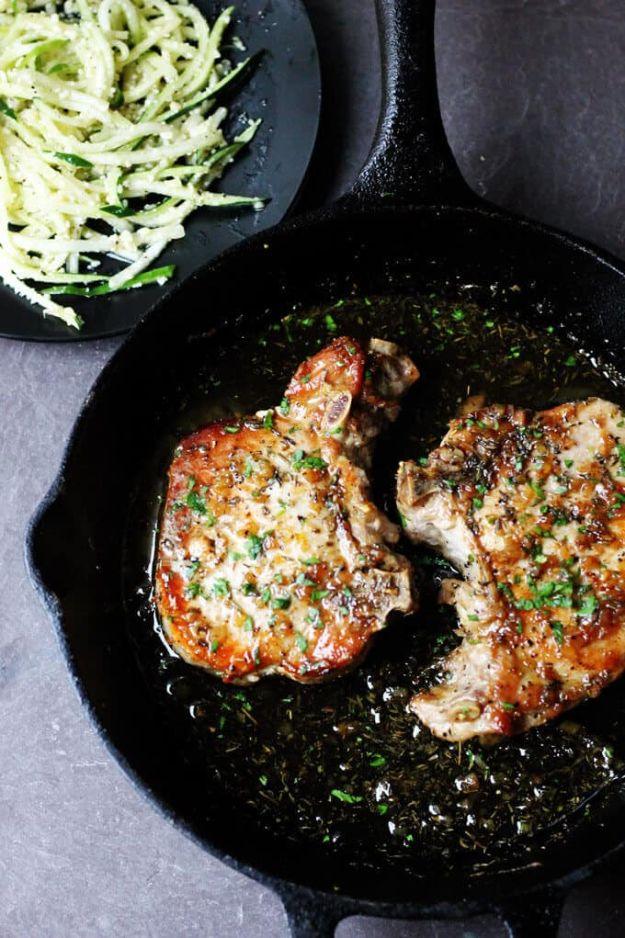 Brown sugar chops with garlic and herbs browned in a cast iron skillet beside a pile of shredded zucchini