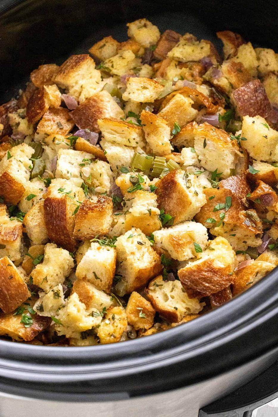 Golden bread-cube stuffing with celery, red onion and herbs fills a black slow-cooker insert in a close-up