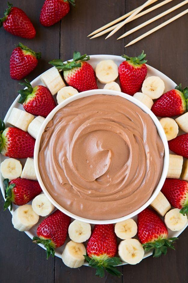 Chocolate fruit dip in a white bowl surrounded by strawberries and banana slices with skewers on the side