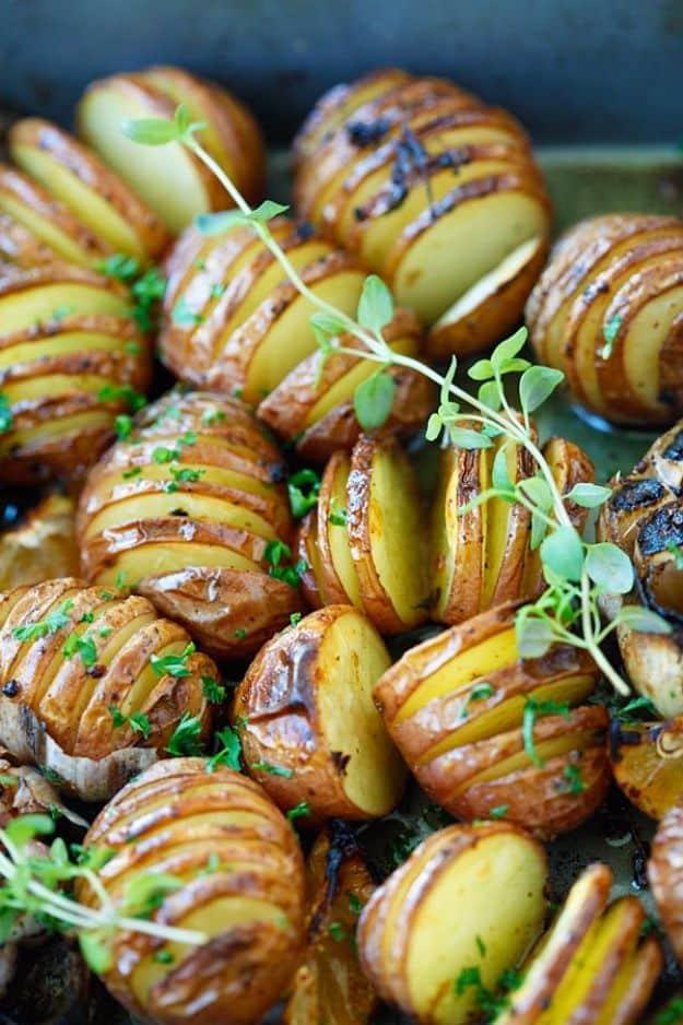 Garlic herb hasselback potatoes on a dark pan, baby potatoes cut in fans with thyme sprigs and roasted garlic