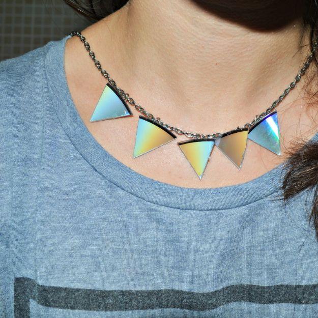 Statement necklace of five iridescent triangles cut from an old CD hanging on a fine chain, worn over a grey striped top