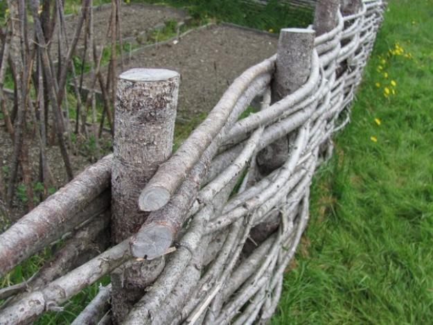 Wattle fencing, thin saplings woven horizontally between cut log posts along the edge of a green lawn and garden bed