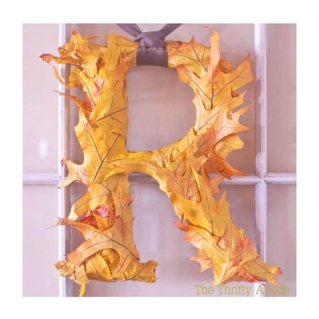 Letter R covered in overlapping orange and yellow artificial oak leaves hanging against a pale lilac window