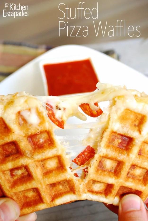 Stuffed pizza waffles pressed in a waffle iron with melted cheese leaking out, served with marinara dip
