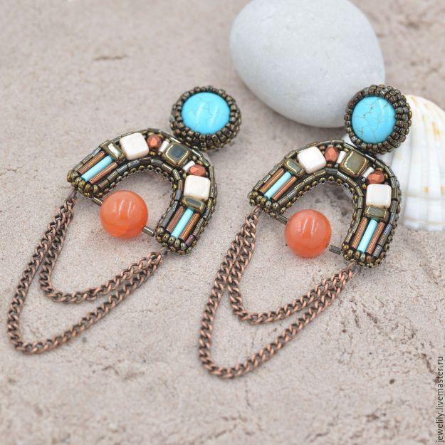 Ethnic beaded earrings, arched bead embroidery panels in turquoise and copper with chain swags, on sand by a shell