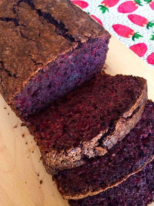 Blackberry bread sliced to show a deep purple crumb, on a wooden board with a strawberry print cloth behind