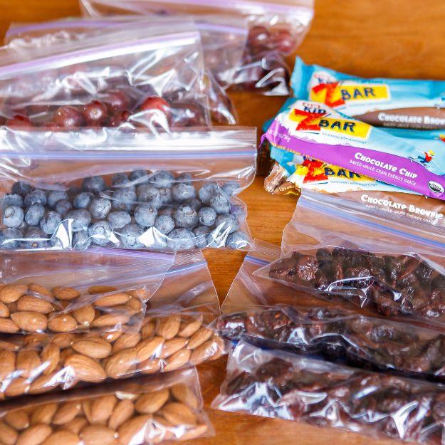 Road trip snacks portioned into zip top bags, grapes, blueberries, almonds and dates beside wrapped snack bars