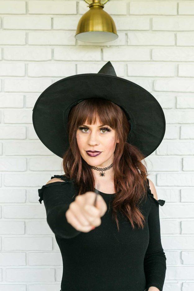 Witch Halloween makeup with smoky purple eyes, dark plum lips, a black witch hat and a spider choker