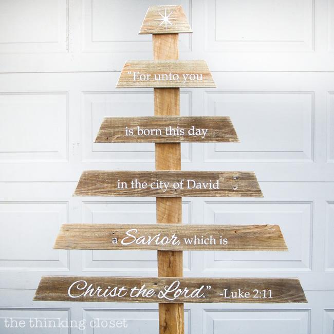 A tall pallet wood tree with six branch boards lettered in white with the Luke 2:11 verse in front of a white garage door