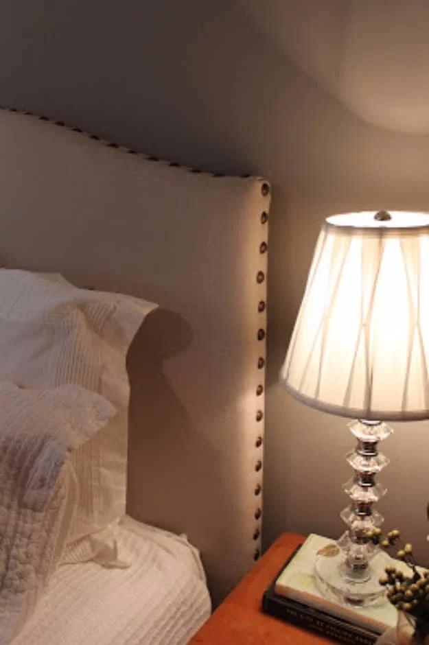 DIY drop cloth headboard, a cream camelback upholstered headboard edged in nailhead trim beside a crystal lamp