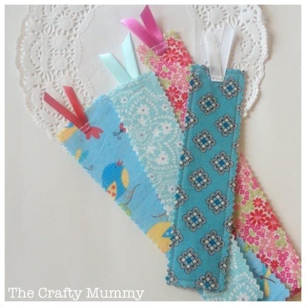 Five fabric scrap bookmarks in blue, pink and floral prints with pinked edges and ribbon tabs, on a white paper doily
