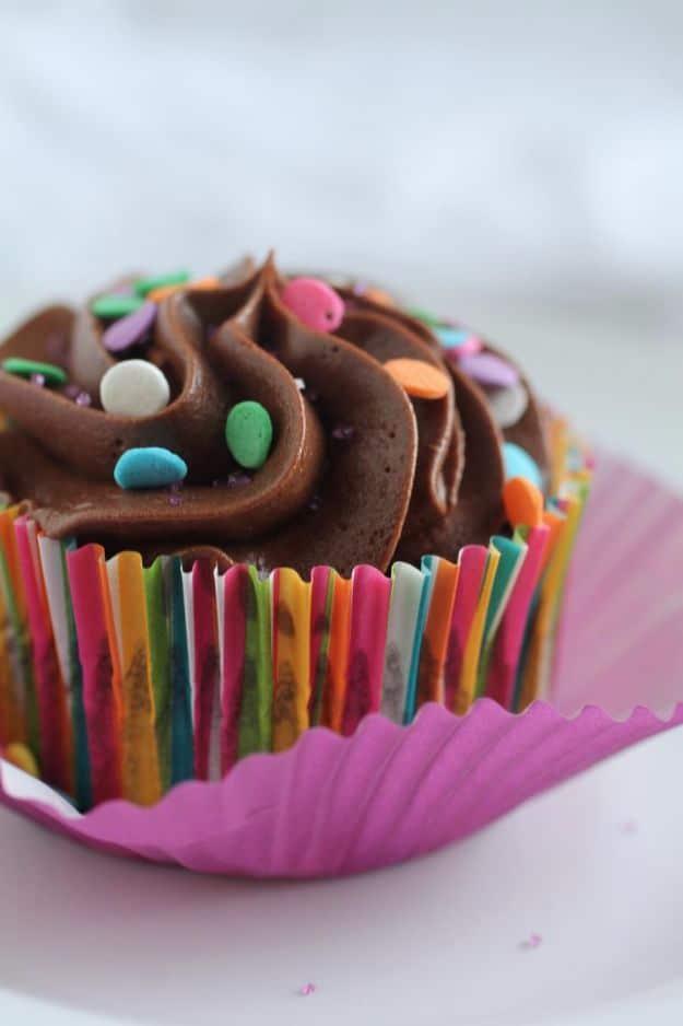 Chocolate frosted cupcake with pastel candy sprinkles in a rainbow striped paper liner on a white plate