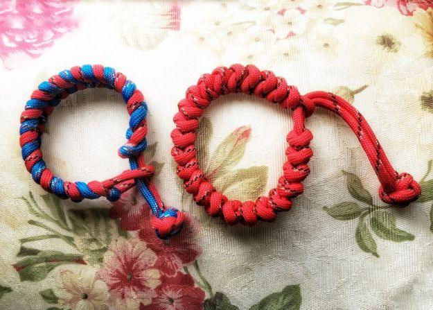 Two red and blue simple cobra knot paracord bracelets with knot closures, laid on floral printed fabric