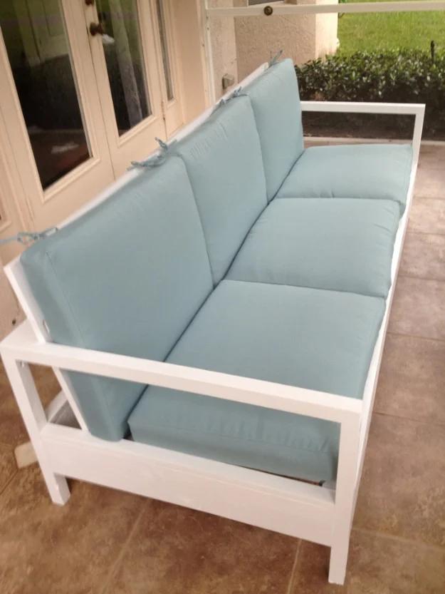 White framed patio sofa with pale blue seat and back cushions on a terracotta patio outside white French doors