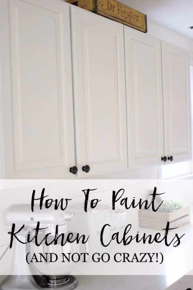 White painted kitchen wall cabinets with black knobs above a counter with a stand mixer and a small crate of greenery