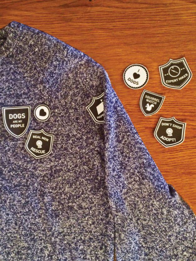 Black and white scout style dog merit badges, several pressed onto a blue sweater sleeve, the rest on a wood table