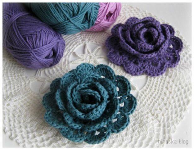 Crochet lace ribbon roses in teal and deep purple lying on a white crocheted doily beside balls of yarn