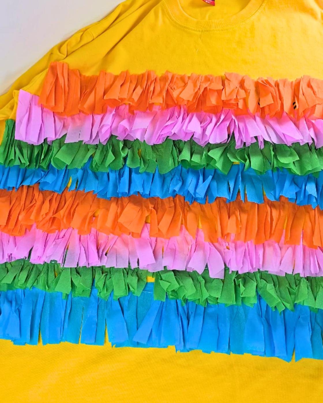 One of the Easiest Halloween Costumes - the finished yellow shirt laid flat, covered in rows of colorful crepe paper fringe.