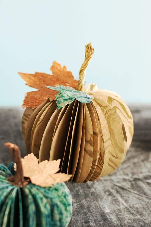 Two folded paper pumpkins in kraft brown and teal with curled stems and cut paper leaves on gray fabric