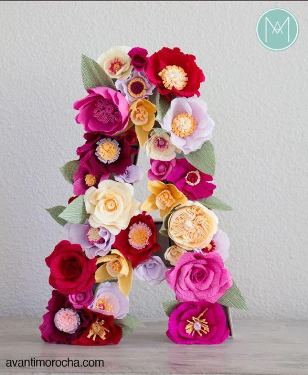Letter A covered entirely in crepe paper roses and anemones in pink, cream, red and gold with green paper leaves
