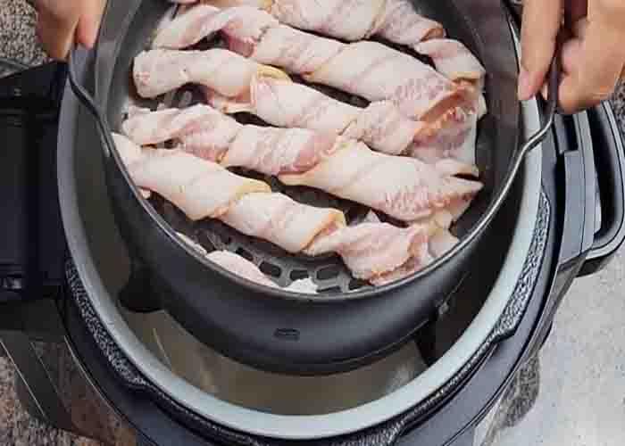 Placing the basket in the air fryer with the twisted bacon