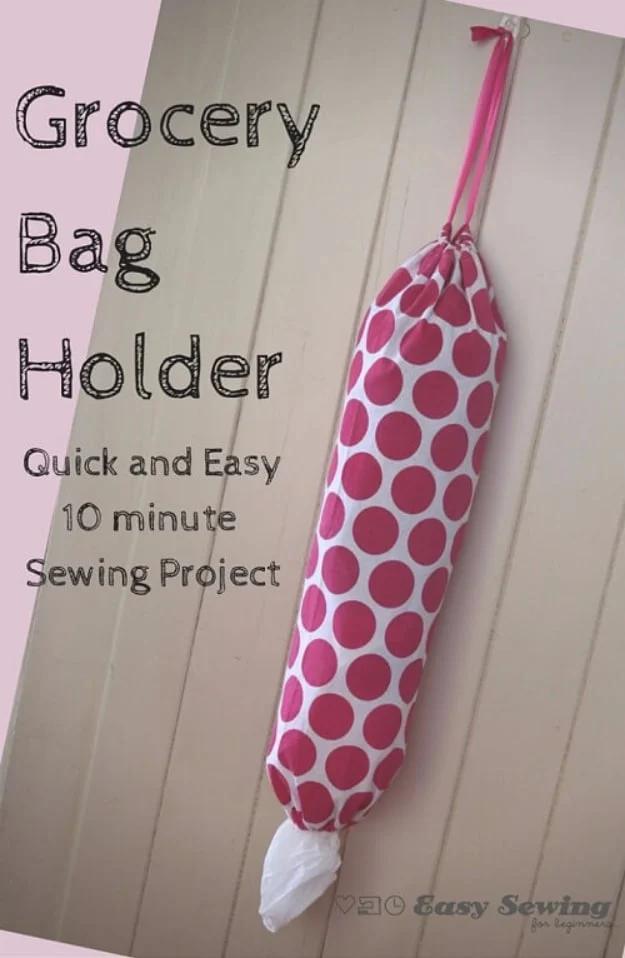 Pink and white spotted fabric grocery bag holder hanging on a wall with a plastic bag pulled out of the bottom