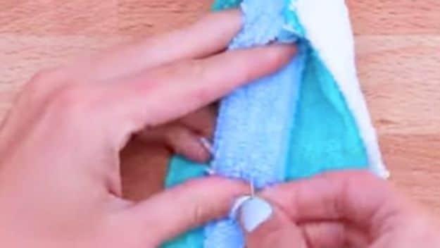 Old towels bath mat tutorial still showing two hands knotting a cut towel strip into a soft bath mat