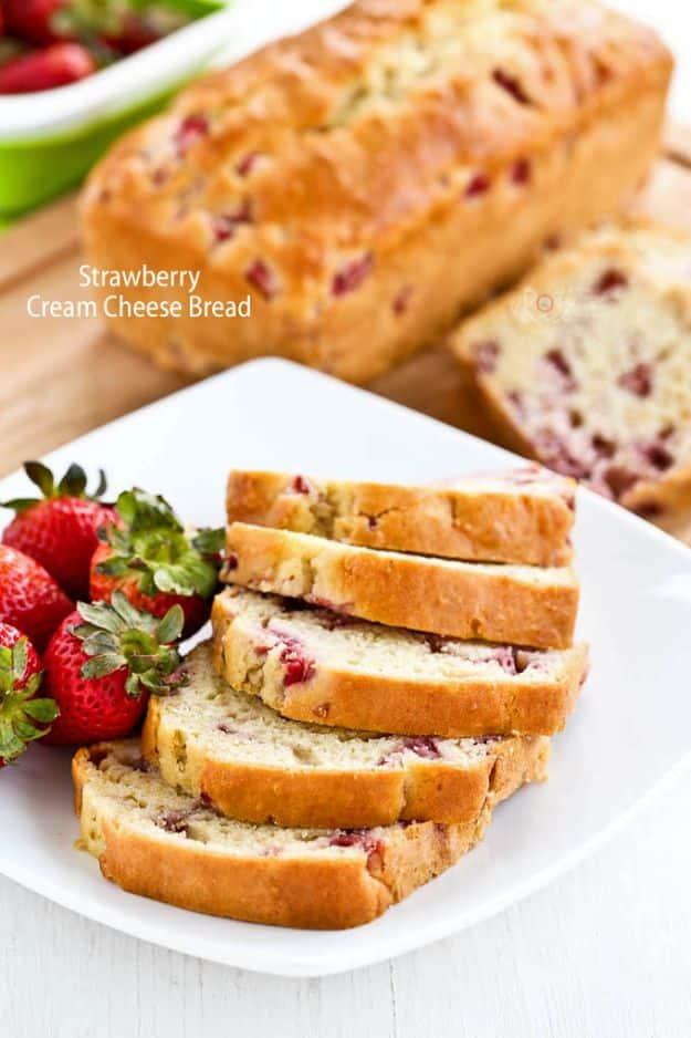 Strawberry cream cheese bread sliced on a white plate with whole fresh strawberries and a second loaf behind