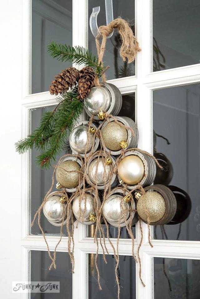 Christmas tree shaped door wreath made from mason jar lid rings tied with twine, each ring holding a gold or silver ornament