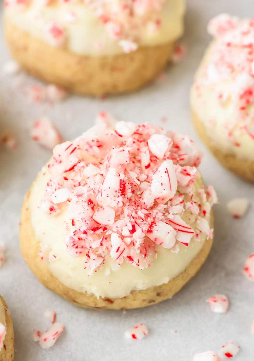 A snowball cookie dipped in white chocolate and coated in crushed candy canes with more cookies and peppermint pieces behind