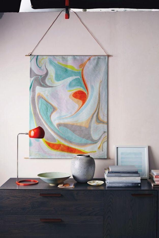 Large marbled paper artwork in pale blue, pink and orange hanging from a cord above a dark sideboard