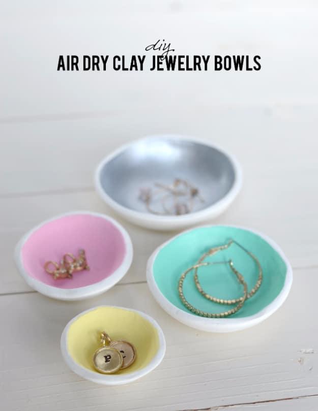 Four small white air dry clay bowls with pink, mint, yellow and silver painted interiors holding rings and earrings
