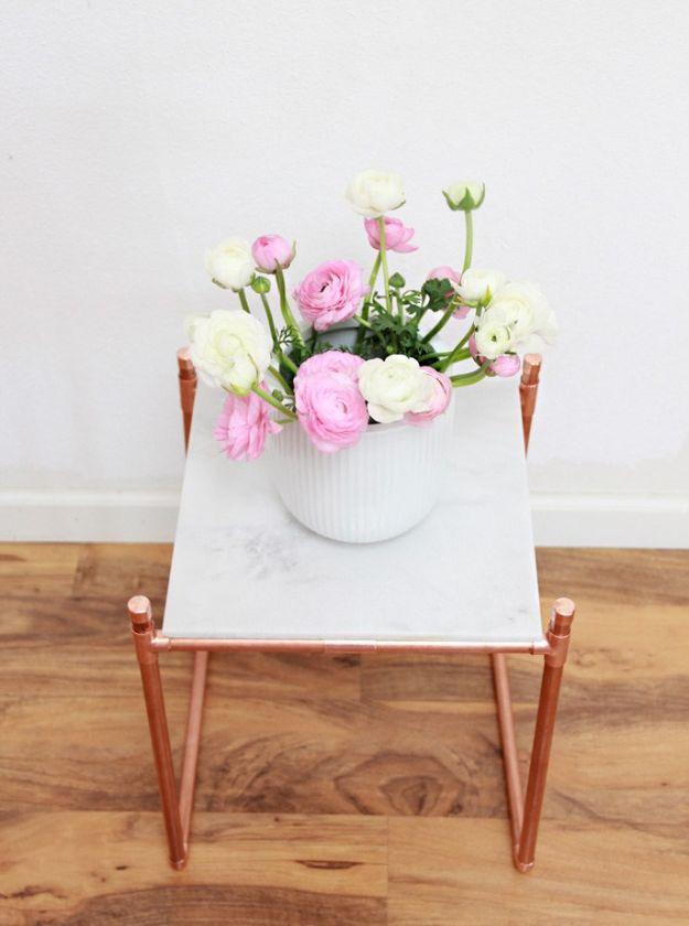 Modern copper pipe plant stand with a white marble tile top holding a bowl of pink and white ranunculus