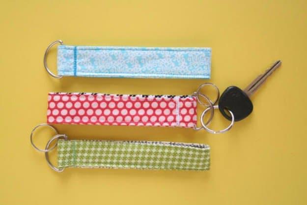 Three fabric key fob wristlets in blue, pink dot and green check prints with silver rings, beside a car key