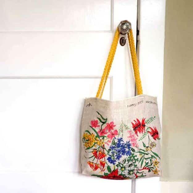Floral linen tea towel sewn into a tote bag with yellow braided straps, hanging from a white painted doorknob