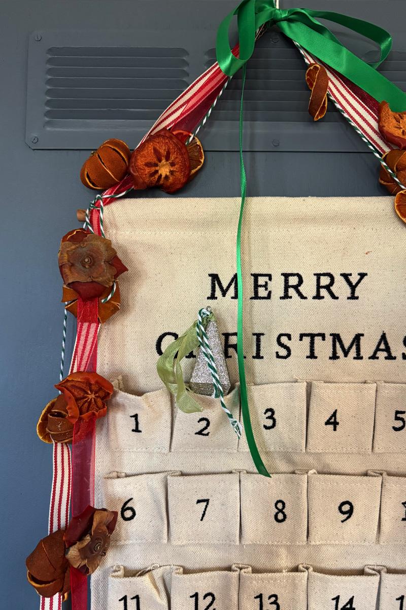 Garland of dried whole persimmons and amber slices on red ribbon draped over a Merry Christmas advent calendar
