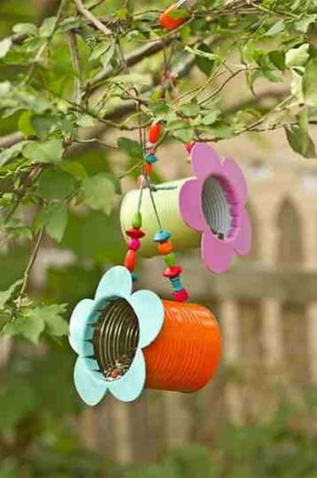 Two tin can bird feeders spray painted orange and green with pink and blue foam flowers, strung on beaded twine in a tree