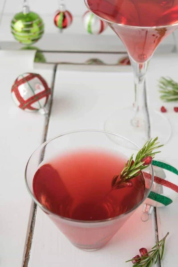 Two glasses of pink cosmopolitan with rosemary sprigs threaded with pomegranate seeds and red and green baubles behind