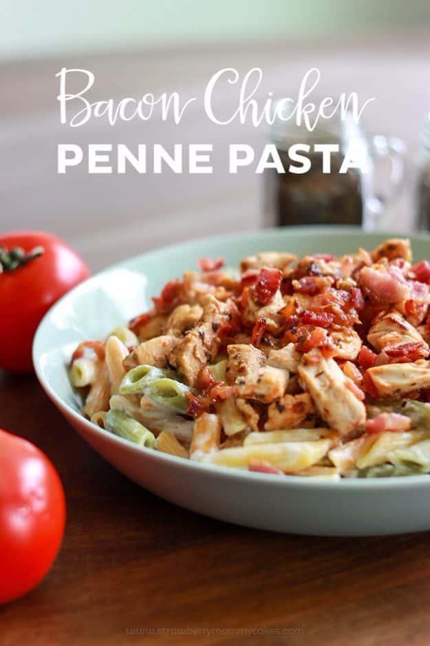 Bacon chicken penne pasta in a pale green bowl with crisp bacon and diced chicken beside two red tomatoes