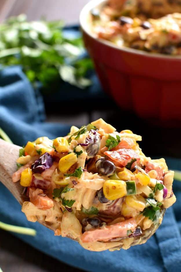 Creamy Mexican coleslaw with charred corn, black beans and cilantro on a wooden spoon above a red bowl