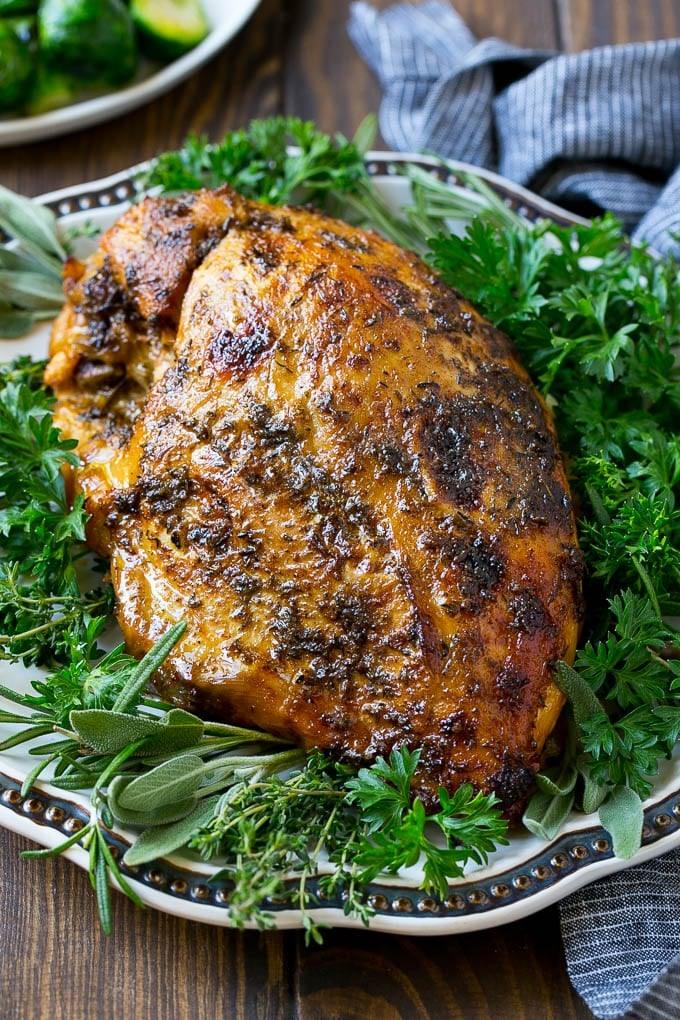 Browned herb-coated turkey breast on a serving platter surrounded by parsley, sage, rosemary and thyme