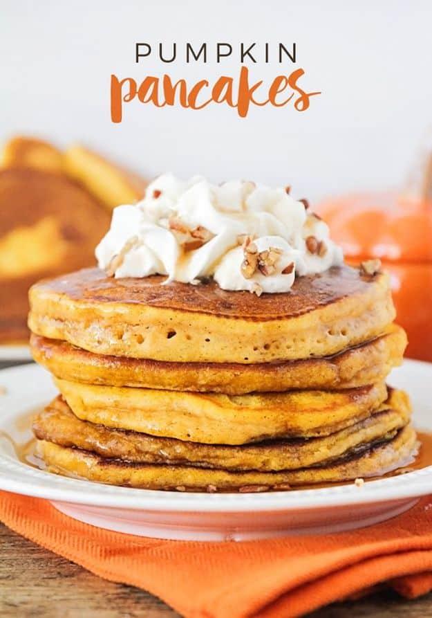 Tall stack of pumpkin pancakes topped with whipped cream and chopped pecans on a bright orange napkin