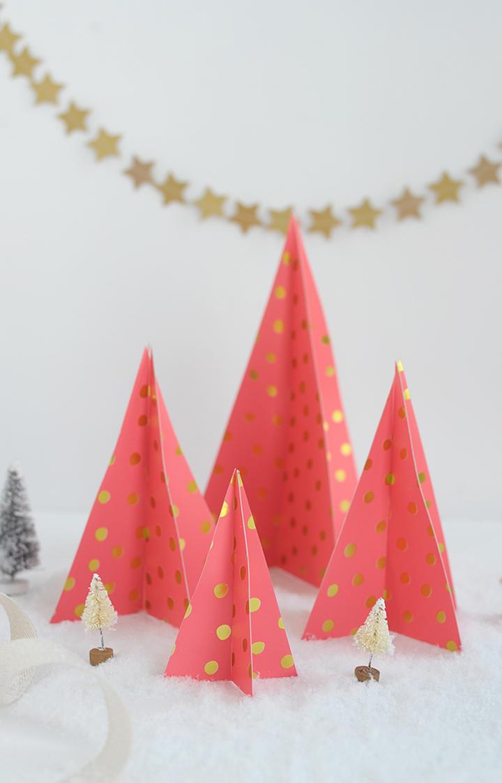 Four coral paper cone Christmas trees with gold polka dots standing in faux snow with a gold star garland strung behind them
