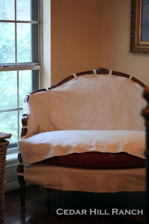 Curved French settee draped with a soft ivory slipcover, photographed in front of a tall window on a wood floor