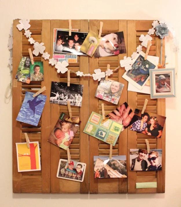 Weathered louvered wooden shutter on a wall covered in clothespins holding photos, postcards and a paper garland