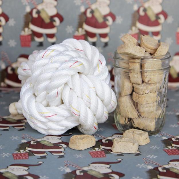 Large white knotted cotton rope ball beside a glass jar of pale dog biscuits on Santa print wrapping paper
