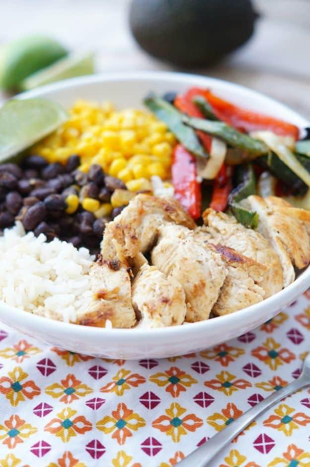 Healthy chicken fajita rice bowl in a white bowl with rice, sliced chicken, peppers, black beans, corn and lime