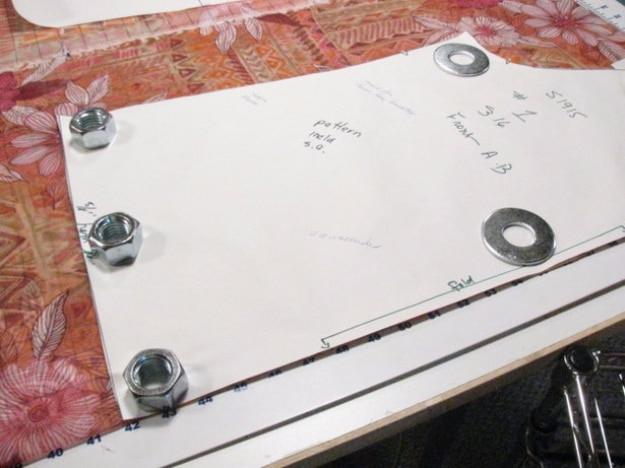 Steel hex nuts and washers holding a paper sewing pattern flat over floral fabric on a cutting table