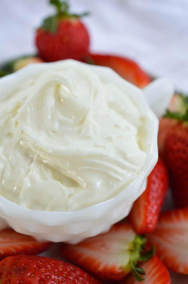 Marshmallow fluff fruit dip in a white bowl beside fresh strawberries and sliced apples ready for dipping